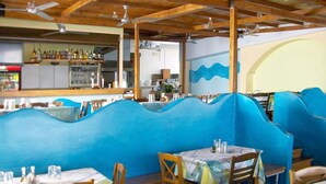 Ein Restaurant mit blauwellenförmigen Sitzgelegenheiten, Holztischen und einer Theke im Hintergrund.