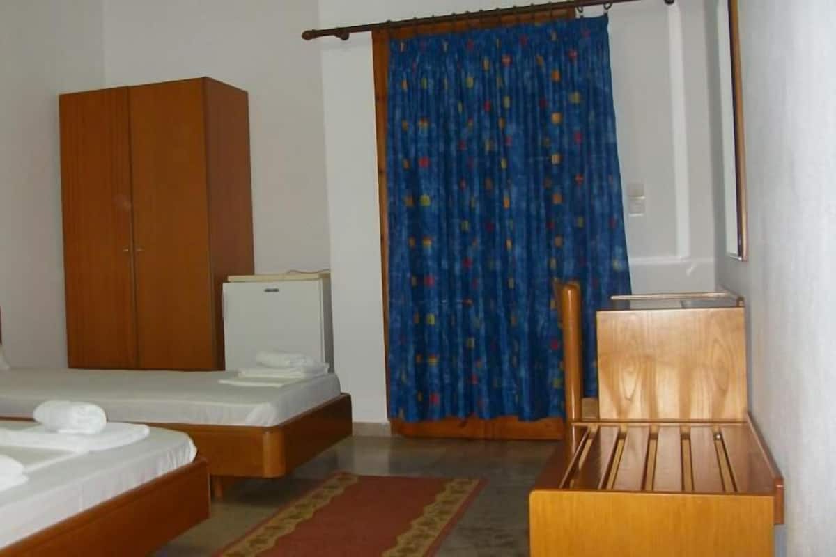A bedroom with a bed, a wardrobe, a small bedside table, and a desk.