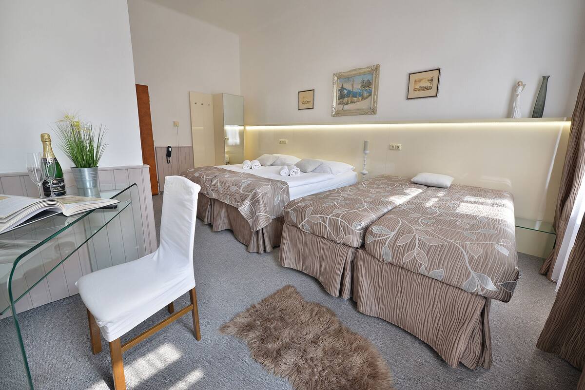Habitación de hotel con dos camas, un escritorio de cristal, una silla, una alfombra mullida y una pared decorada con marcos.