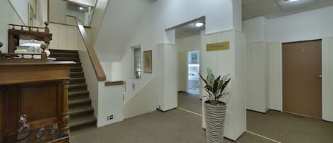 A spacious lobby with a wooden staircase, a reception desk, and a potted plant.