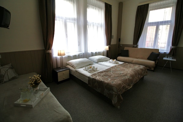 A hotel room with a large bed, a sofa, a small table, and a TV.