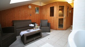 Quarto com painéis de madeira, um sofá, cadeiras, uma mesa de centro e uma sauna com paredes de vidro.