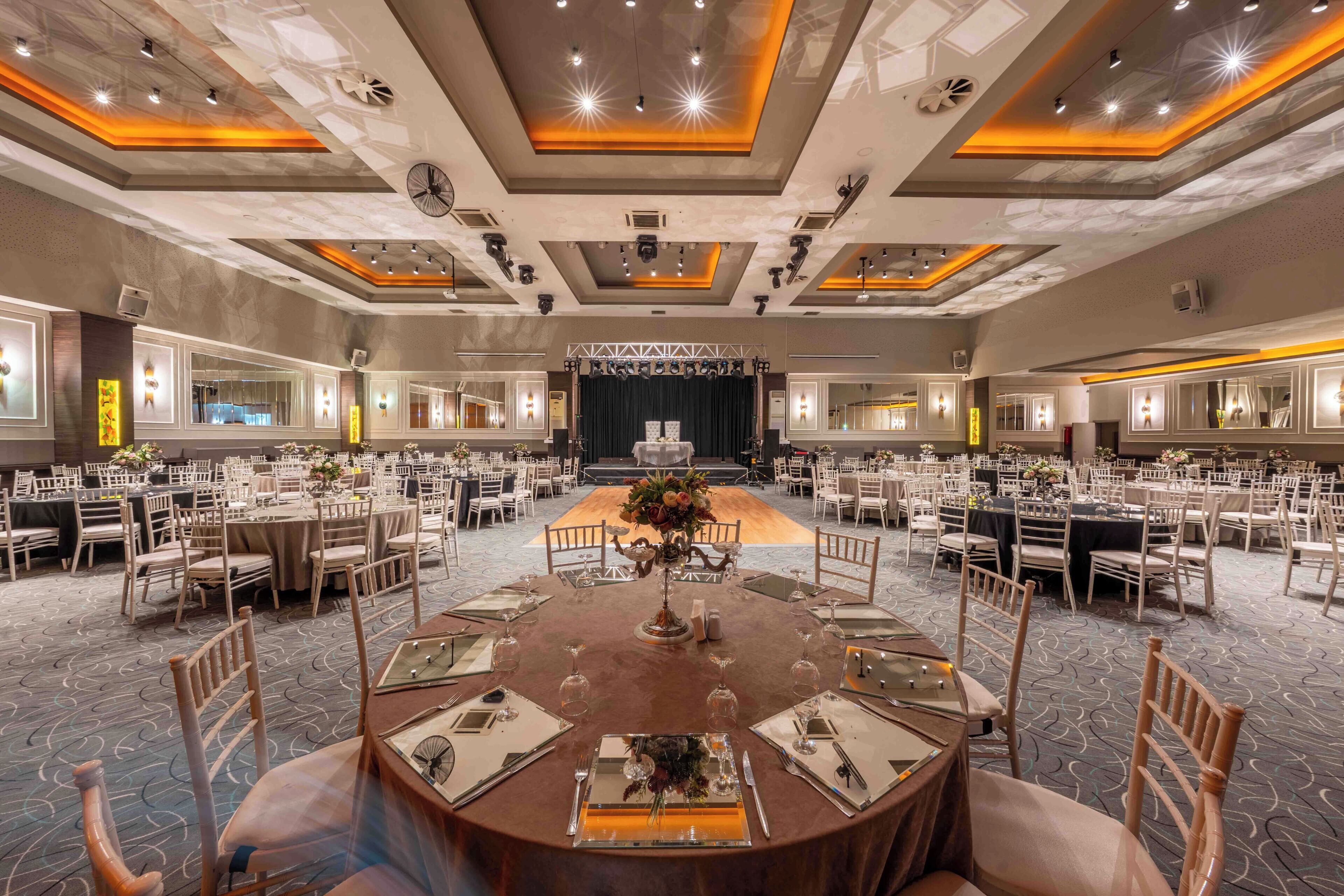 A large banquet hall with round tables, chairs, and a stage.