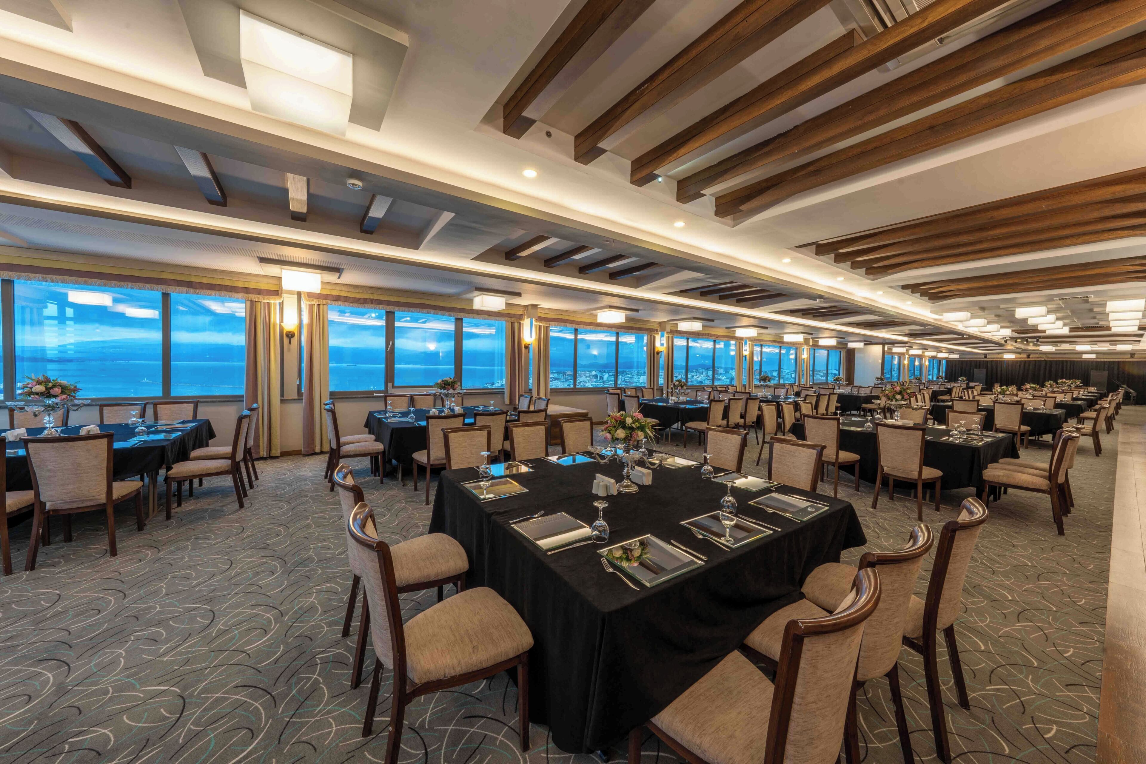 A conference room with tables and chairs, large windows with a view, and a modern ceiling design.