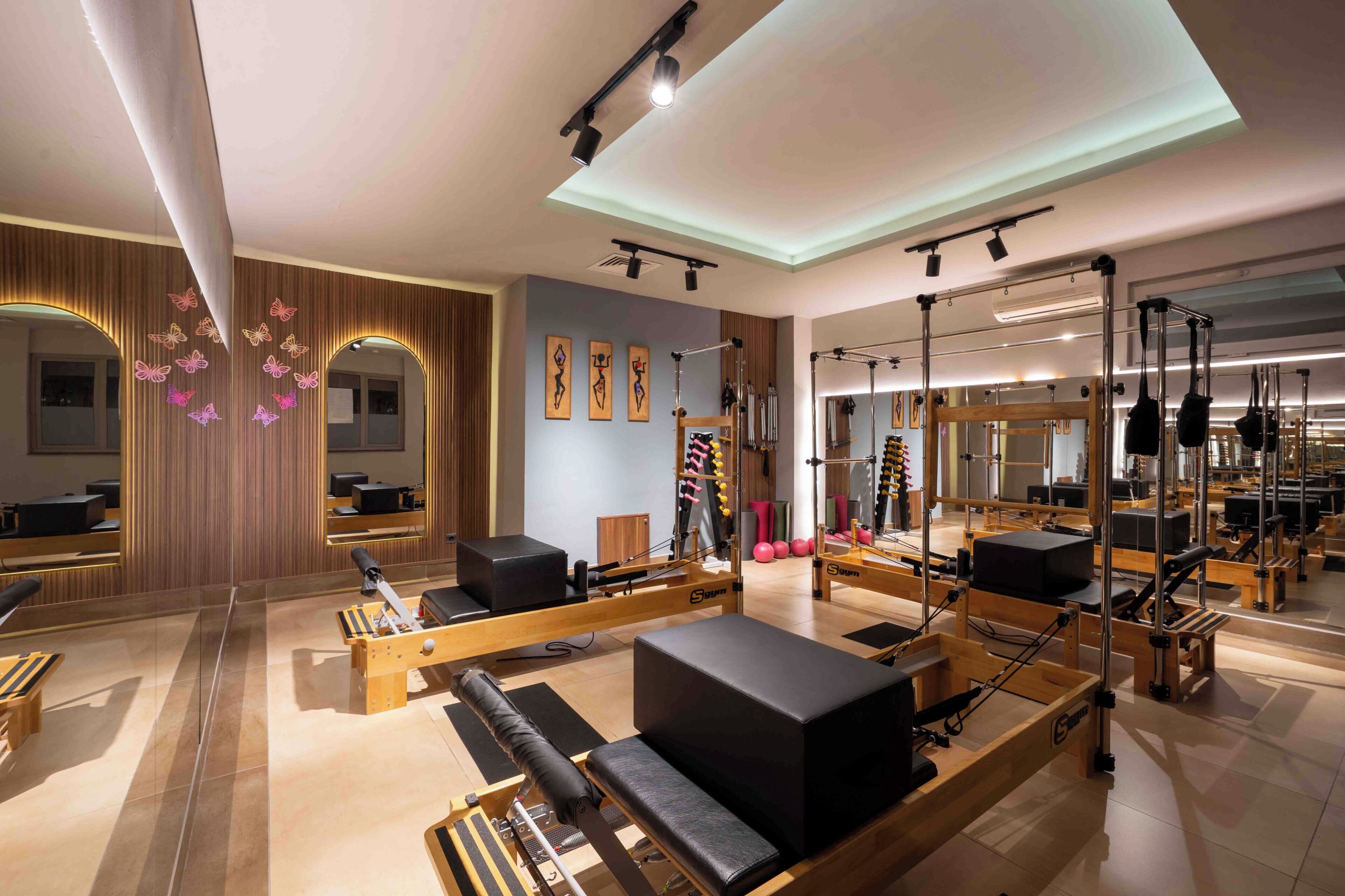 Un estudio de Pilates con paredes de espejo, equipo de madera y un diseño de techo moderno.