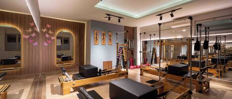 Un estudio de Pilates con paredes de espejo, equipo de madera y un diseño de techo moderno.