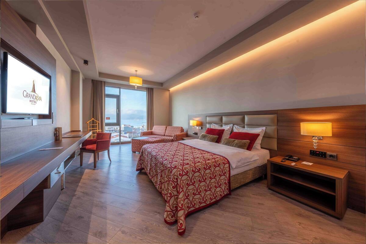Ein Hotelzimmer mit Bett, Schreibtisch, Stuhl, Fernseher und Blick auf die Stadt.