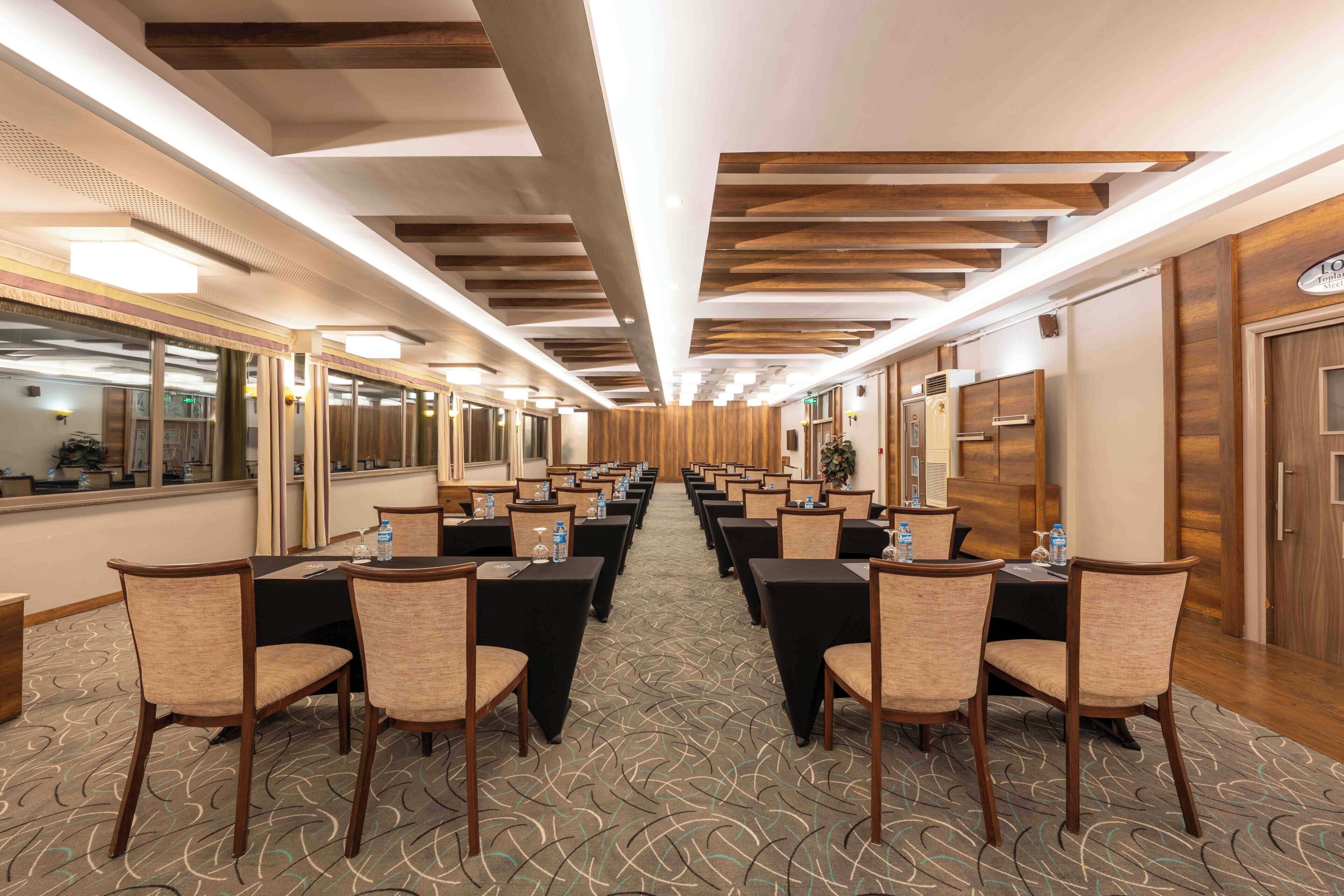 Een hotelconferentieruimte met rijen tafels en stoelen, houten paneelwanden en een kamerbreed tapijt met patroon.