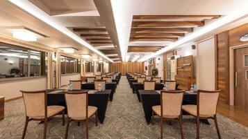 Een hotelconferentieruimte met rijen tafels en stoelen, houten paneelwanden en een kamerbreed tapijt met patroon.