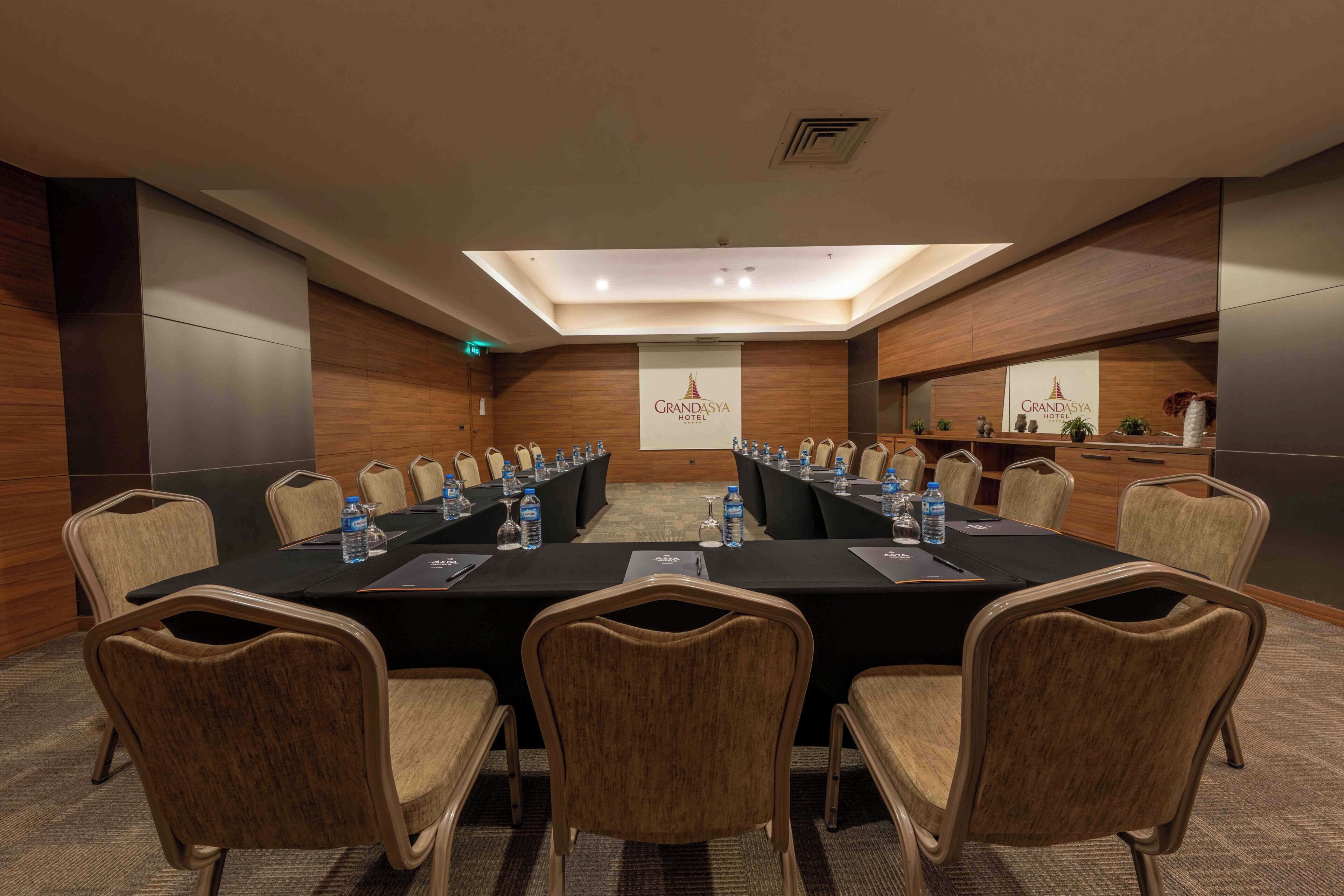 A conference room with a long table, chairs, water bottles, and a banner reading 'Grandasa Hotel.'