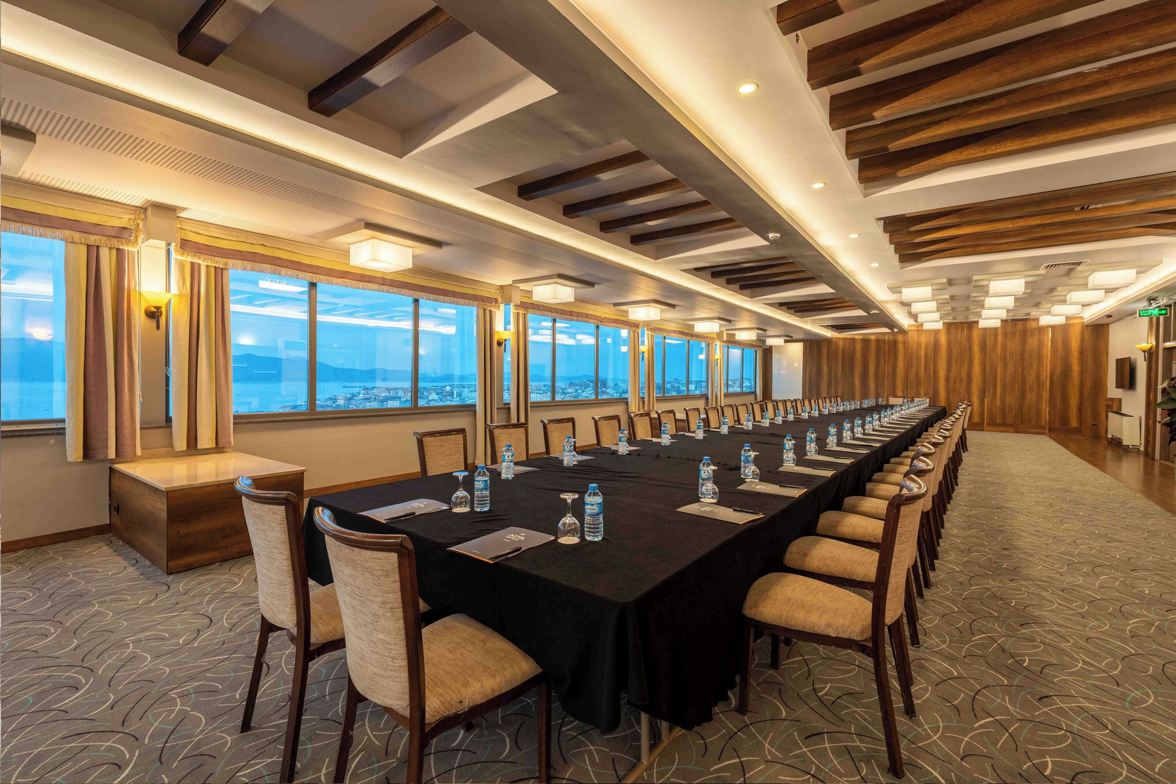 A conference room with a long table, chairs, and a city view through large windows.