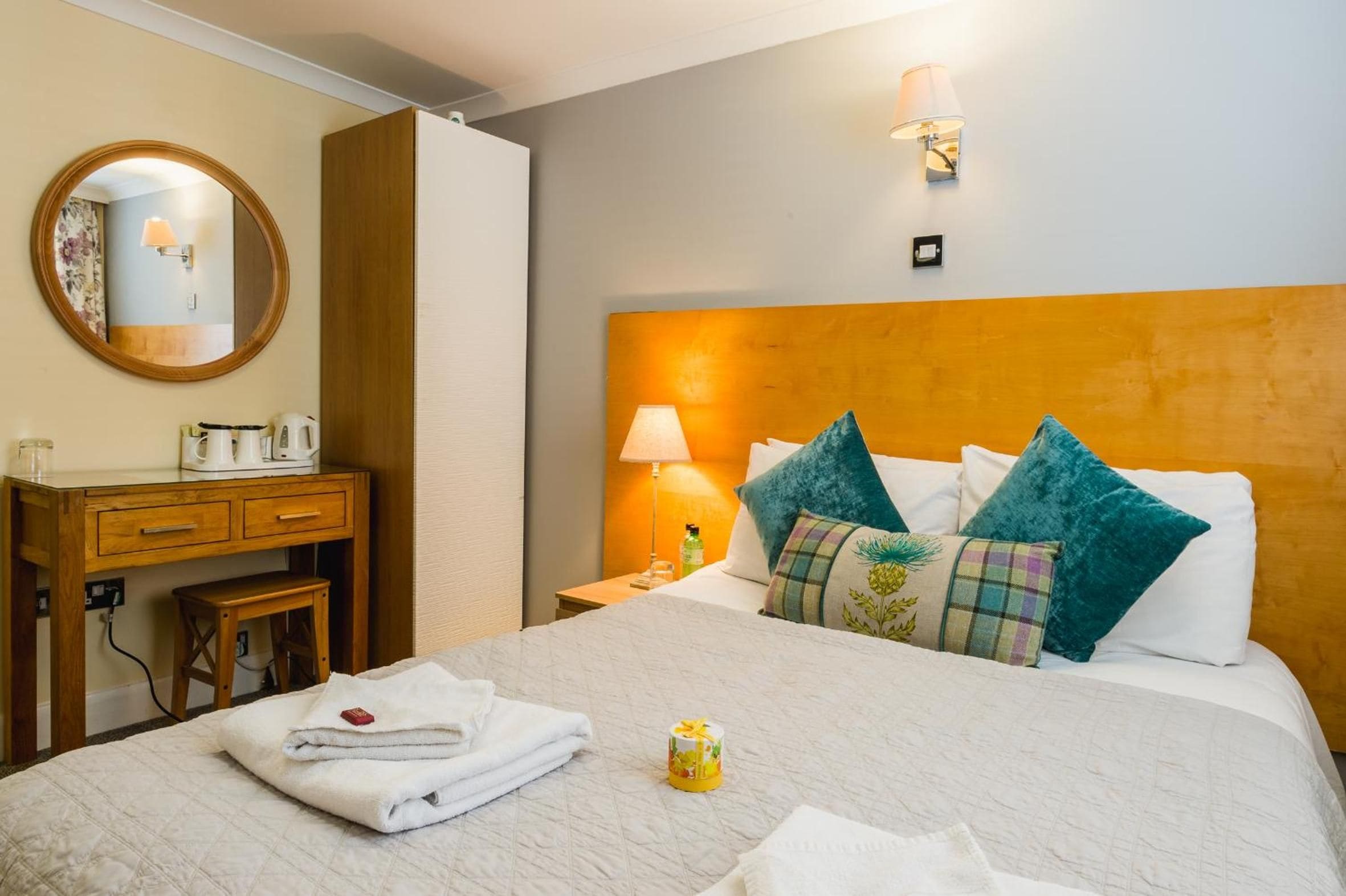 A hotel room with a bed, a bedside table, a lamp, a mirror, and a wooden dresser.