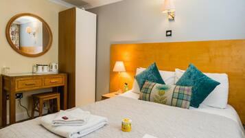 A hotel room with a bed, a bedside table, a lamp, a mirror, and a wooden dresser.