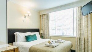 A hotel room with a bed, a desk, a TV, and a window with curtains. - George Oxford Hotel (Oxford)