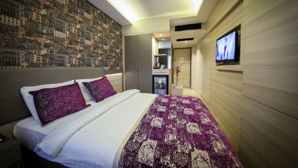 Une chambre d’hôtel moderne avec un grand lit, un téléviseur fixé au mur et une fresque représentant un paysage urbain sur le mur.