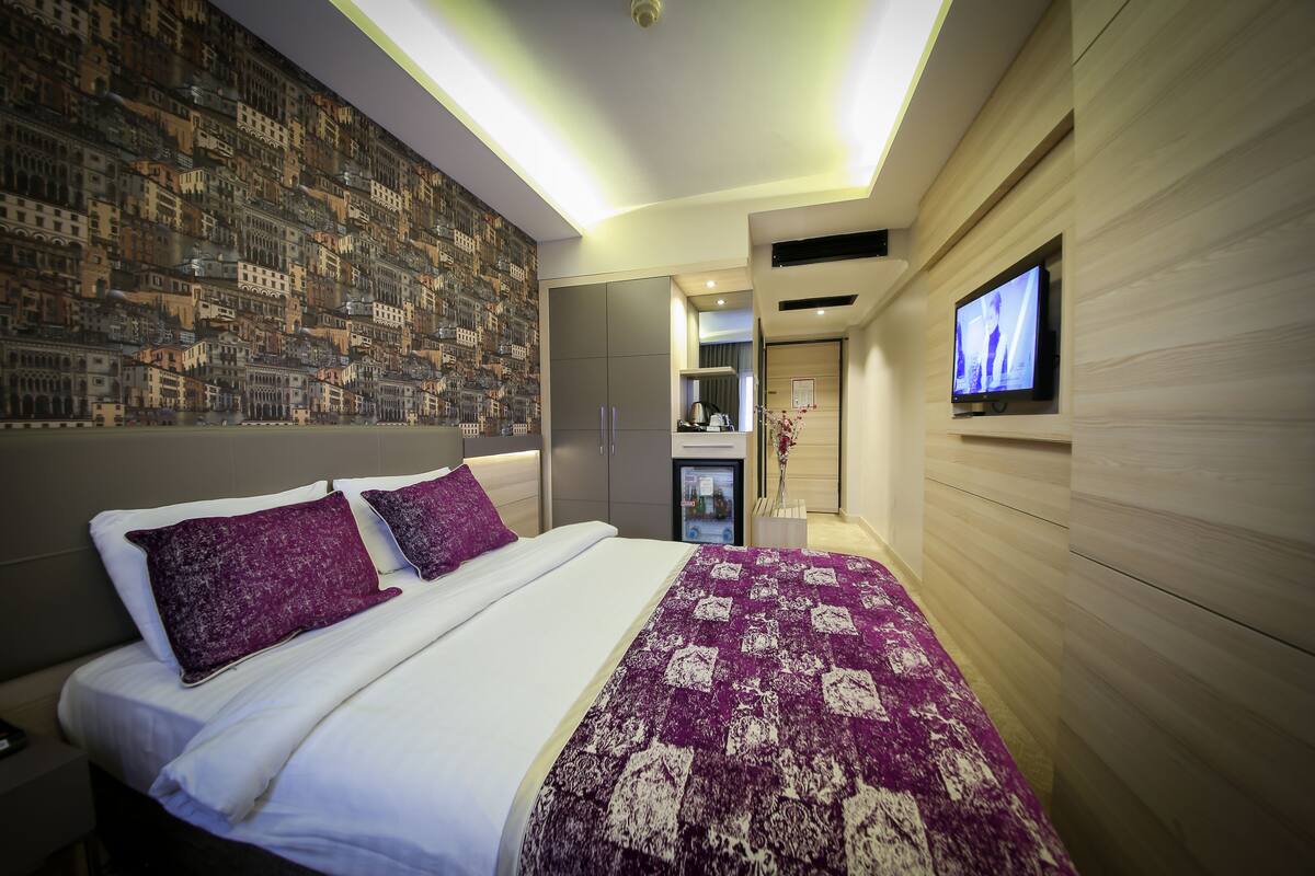 Una habitación de hotel moderna con una cama grande, un televisor fijado a la pared y un mural con un paisaje urbano.