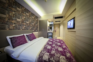Una habitación de hotel moderna con una cama grande, un televisor fijado a la pared y un mural con un paisaje urbano.