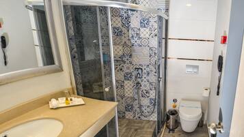 Un baño con cabina de ducha de vidrio, lavabo con artículos de aseo y retrete.