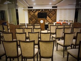 Un salón de conferencias con filas de sillas, un atril y una pantalla grande.