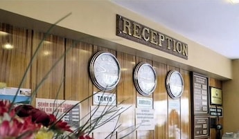 Zona de recepción con un cartel que dice 'RECEPTION', tres relojes y algunos carteles informativos.