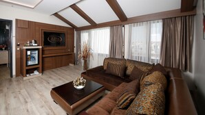 Una sala de estar moderna con un sofá marrón, una mesita de centro, un televisor montado en una pared de madera y un minibar.