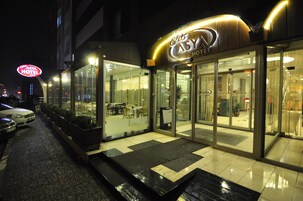 Entrada de hotel con puertas de vidrio, un letrero de neón y un camino pavimentado.