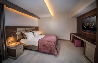Una habitación de hotel moderna con una cama, mesita de noche, televisor y una mesita auxiliar de madera.
