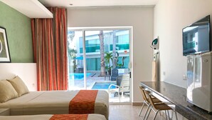 Habitación de hotel con dos camas, kitchenette, televisor y vista a una piscina y un edificio.