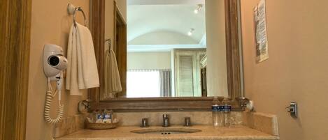 Un baño con un espejo grande, un secador de pelo, una toalla, un lavabo y un ventanal pequeño.