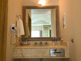 Un baño con un espejo grande, un secador de pelo, una toalla, un lavabo y un ventanal pequeño.