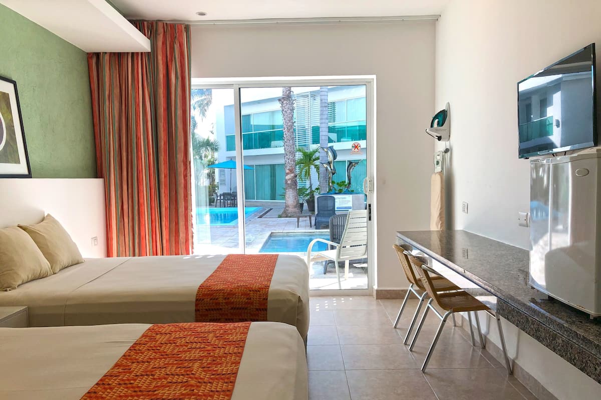 Habitación de hotel con dos camas, zona de comedor, televisor y vista a una piscina.