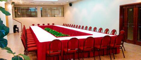 A conference room with a long table, red chairs, and a green plant centerpiece.