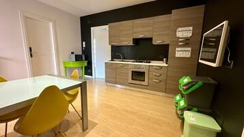 A compact kitchen with a built-in oven, a sink, and a stove. There is a dining table with chairs and a small green table with a microwave.