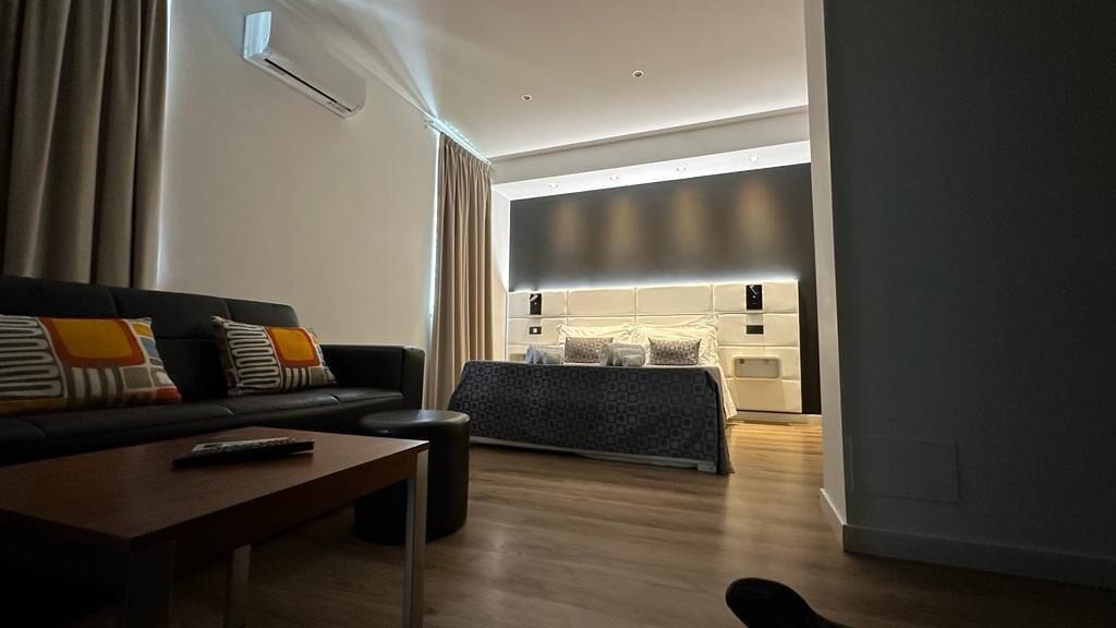 Una habitación de hotel moderna con sofá, una mesita de centro, una cama con cabecero y un equipo de aire acondicionado.