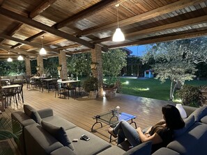 Eine Terrasse im Freien mit Holzboden, Sitzbereichen und hängenden Pendelleuchten.