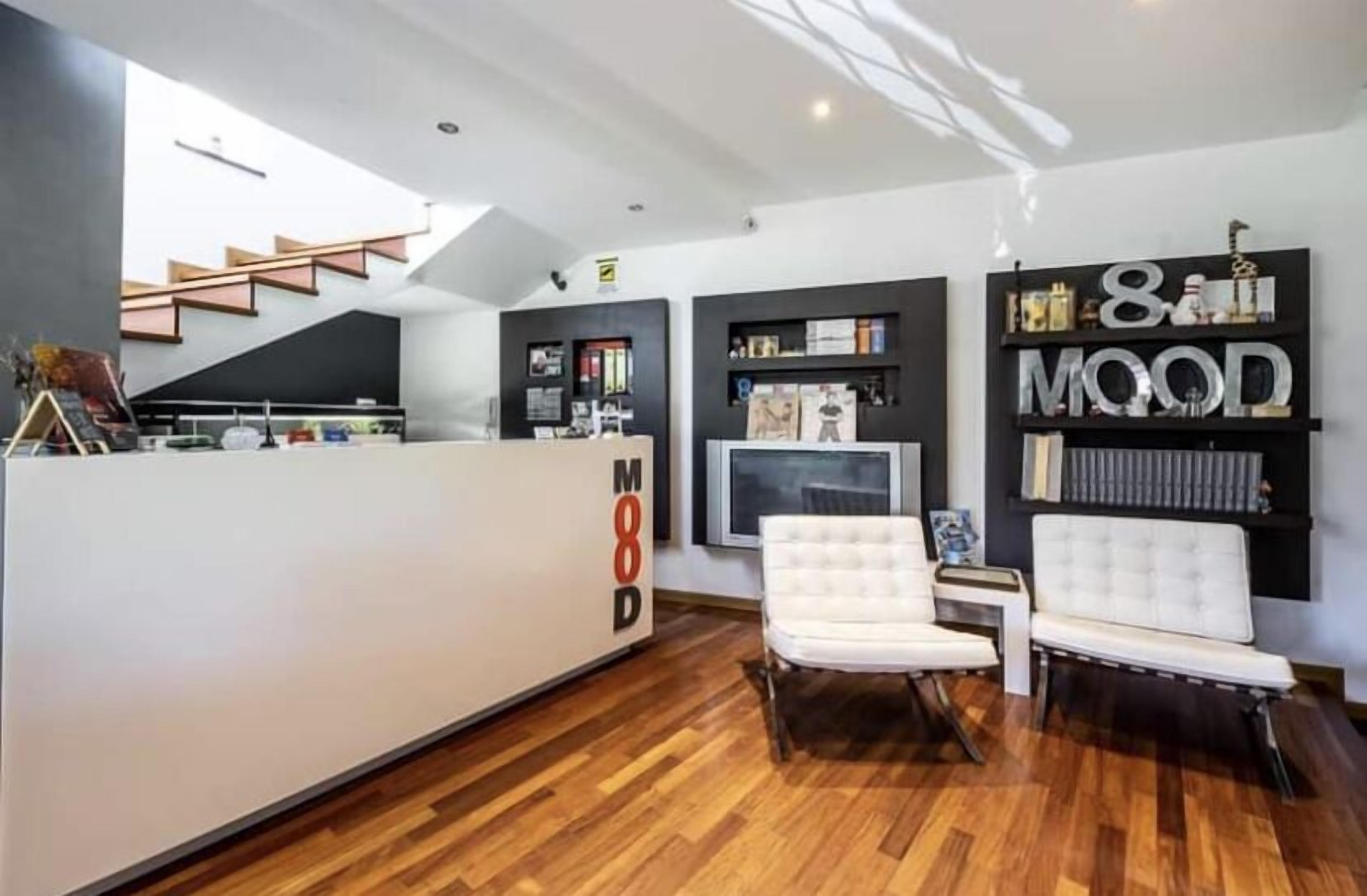 Een modern interieur met een receptiebalie, een trap en een zithoek met een witte bank en fauteuils.