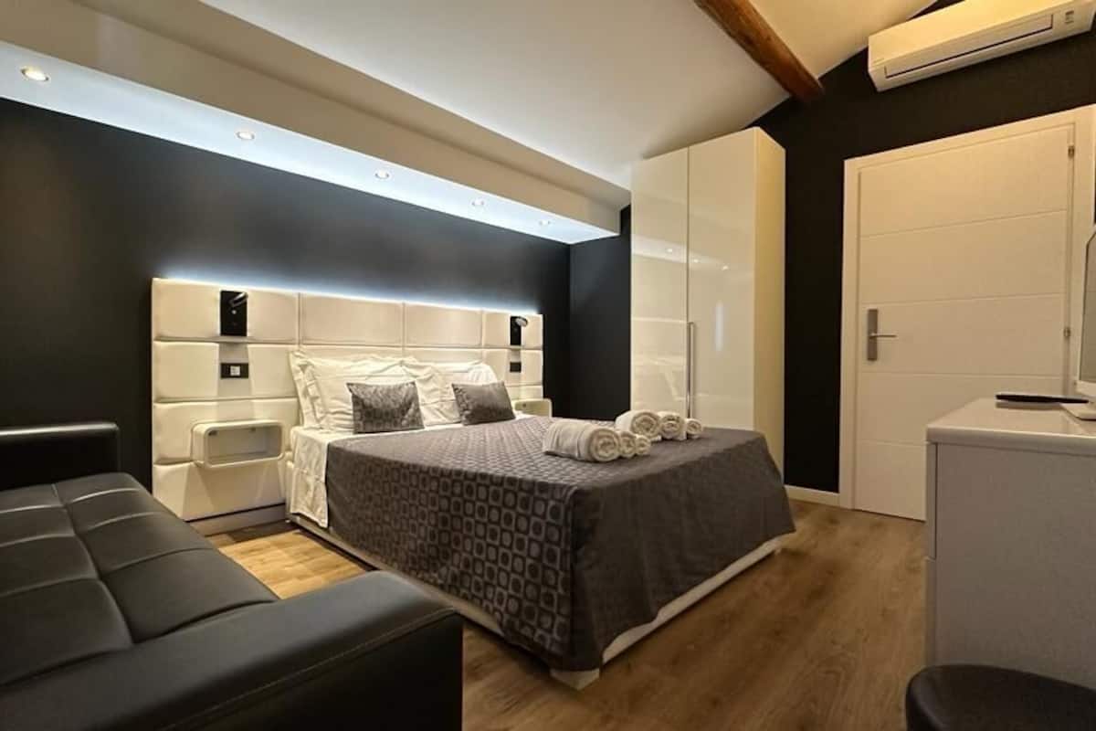 A modern bedroom with a large bed, bedside tables, a sofa, and a small desk.