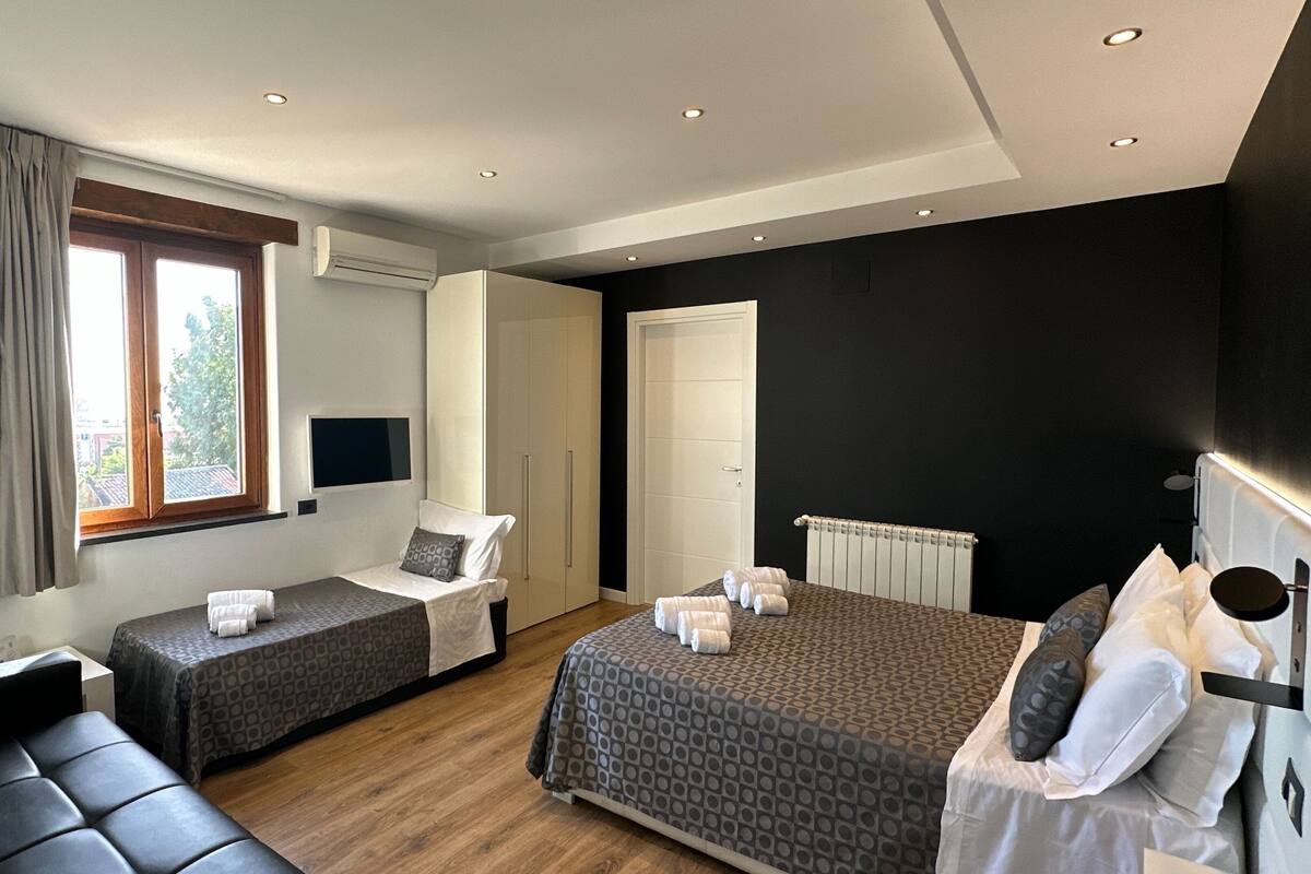 A modern hotel room with two beds, a sofa, a TV, and a window with curtains.