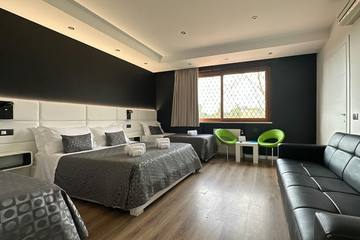 A modern hotel room with a large bed, two smaller beds, a sofa, a dining table, and two chairs.