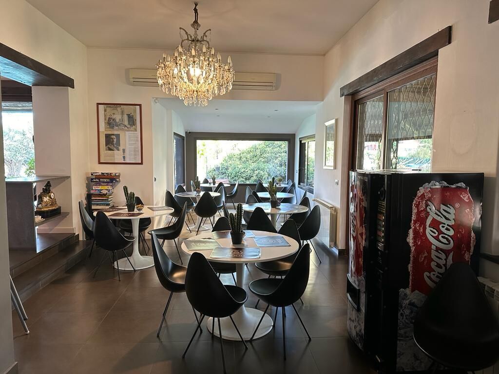 Un comedor con varias mesas redondas y sillas negras, un candelabro y una máquina expendedora de Coca-Cola.