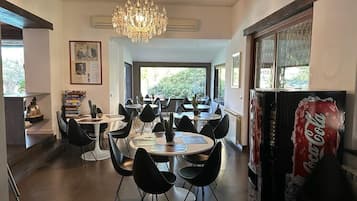 Un comedor con varias mesas redondas y sillas negras, un candelabro y una máquina expendedora de Coca-Cola.