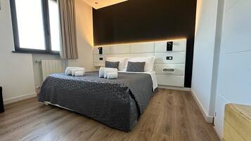 A modern bedroom with a large bed, a headboard with built-in lighting, and a window with curtains.