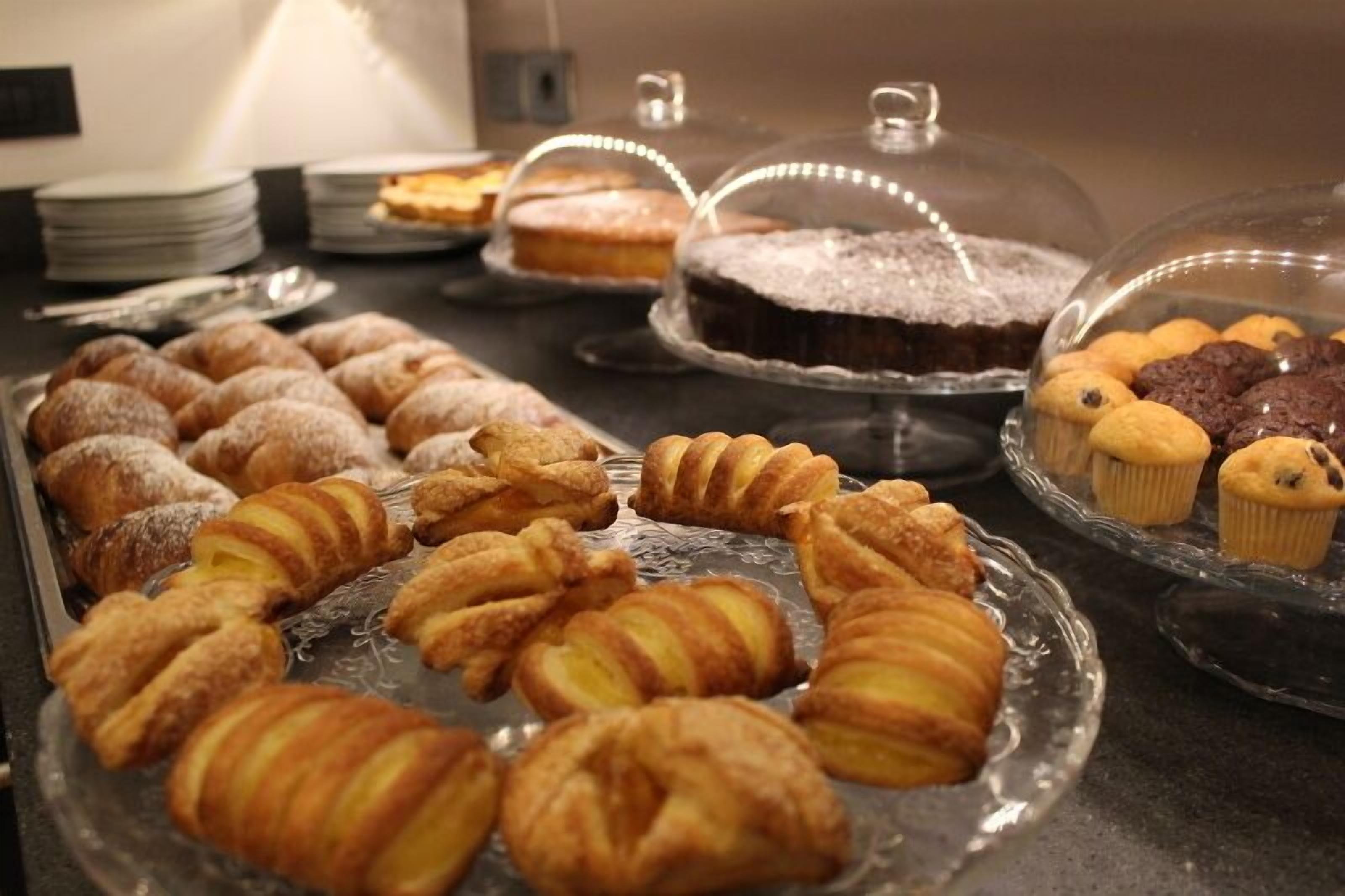 Un buffet proposant une variété de viennoiseries et de desserts, notamment des croissants et des muffins, présentés sur des assiettes en verre et sous des cloches de verre.