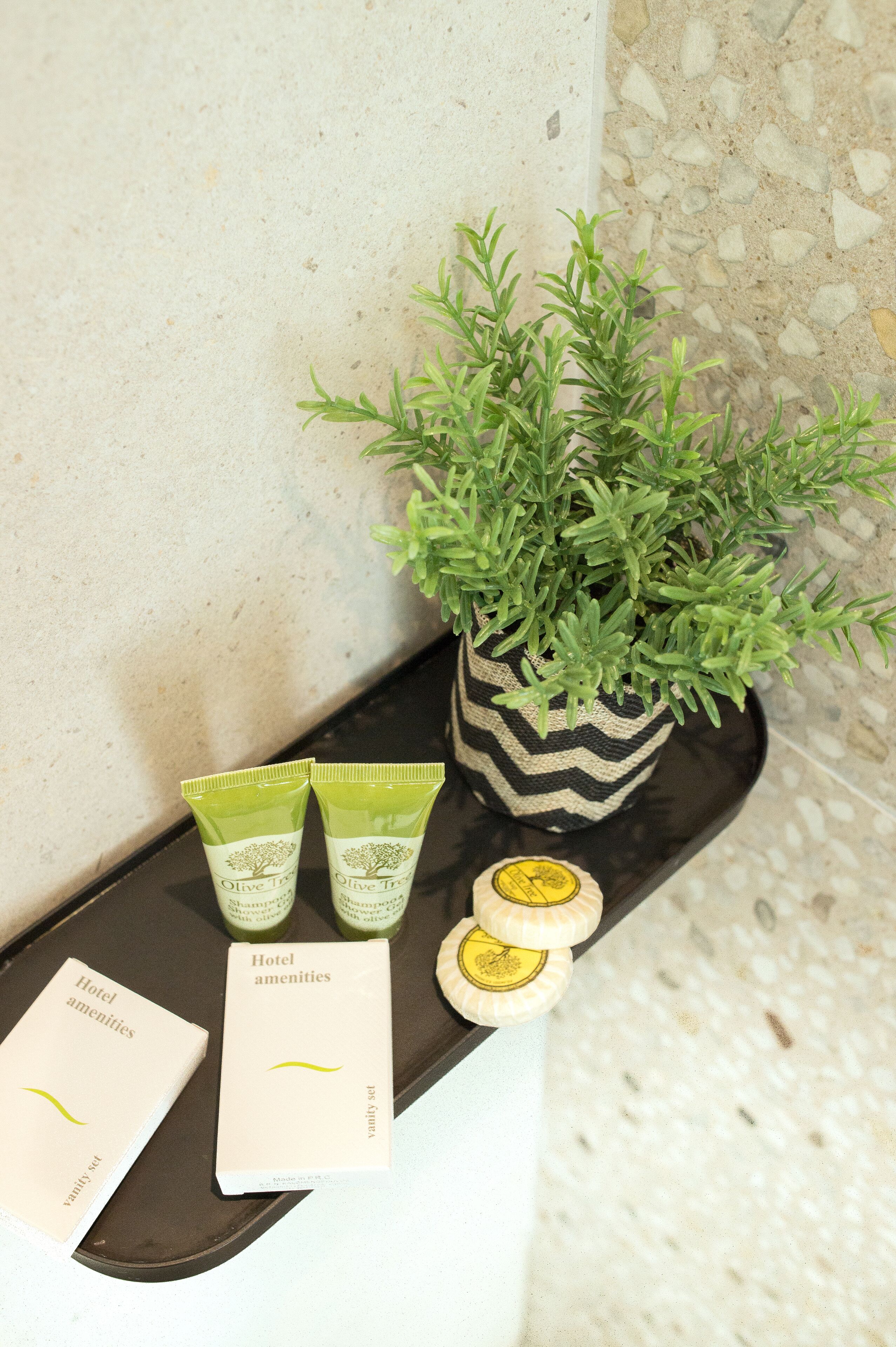 Un plateau contenant deux tubes de crème à l’huile d’olive, une bouteille d’huile d’olive et un ensemble de cartes présentant les produits d’accueil de l’hôtel.