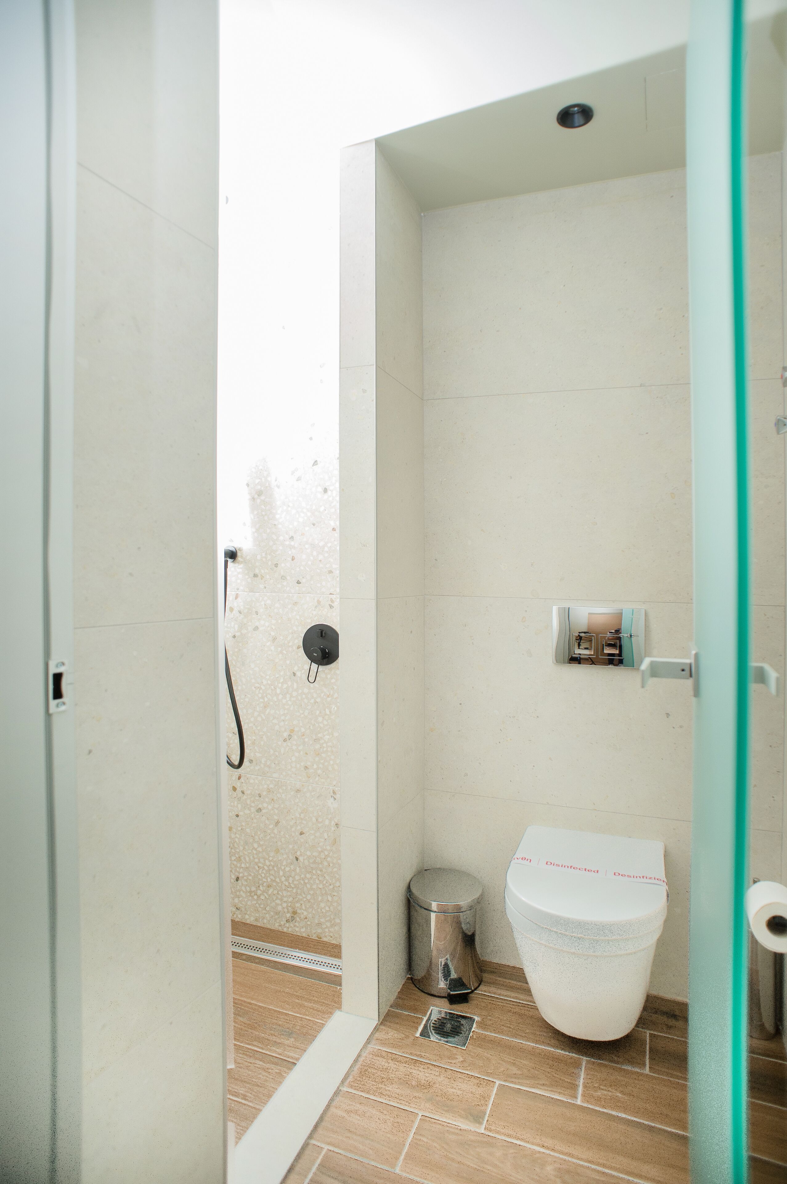 A small, enclosed bathroom with a toilet, a trash bin, and a shower area.