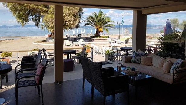 En overdækket udendørs siddeplads med fletmøbler og en sofa, med udsigt over en strand og havet.