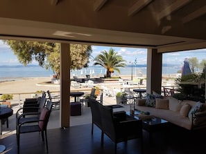 Un espacio de descanso al aire libre techado, con mobiliario de mimbre y un sofá, con vistas a una playa y al mar.