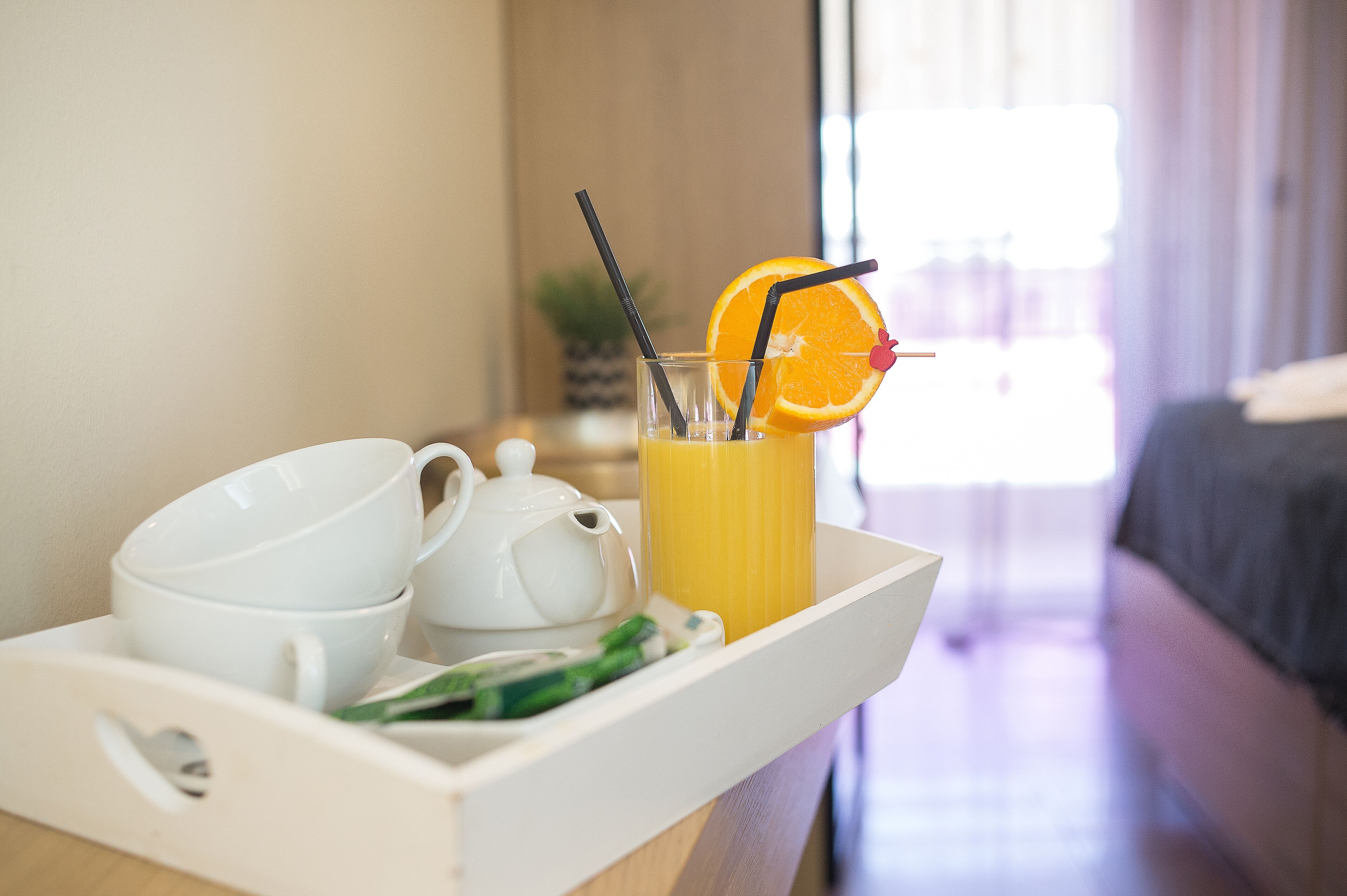 Bandeja de desayuno con tetera, tazas, vaso de jugo de naranja y una rodaja de naranja.