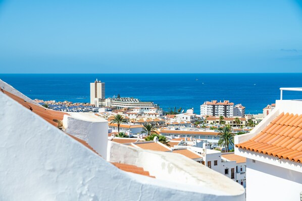A coastal cityscape with white buildings, a prominent tower, and the sea in the background.