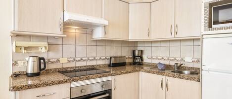 A kitchen with light wood cabinets, a built-in oven, a microwave, a toaster, and a kettle on the countertop.